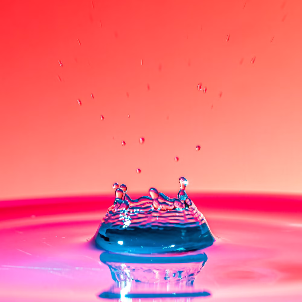 Colorful Water Splash Crown With Blue Droplet Reflection On Pink Gradient Background