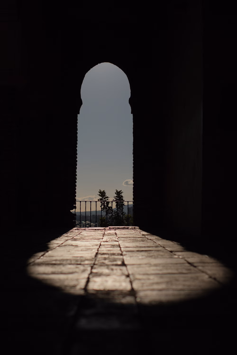 Sunlit Archway Over Tiled Floor With Balcony View and Dramatic Shadowed Doorway