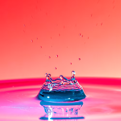 Colorful Water Splash Crown With Blue Droplet Reflection On Pink Gradient Background