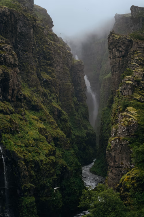 Misty Canyon Waterfall Flowing Through Moss-Covered Cliffs Into a Narrow River Gorge