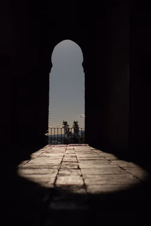 Sunlit Archway Over Tiled Floor With Balcony View and Dramatic Shadowed Doorway