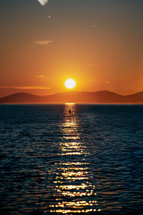 Sunset Paddleboard Silhouette on Ocean With Golden Reflection and Distant Hills